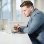 Man sitting on a desk working on a laptop